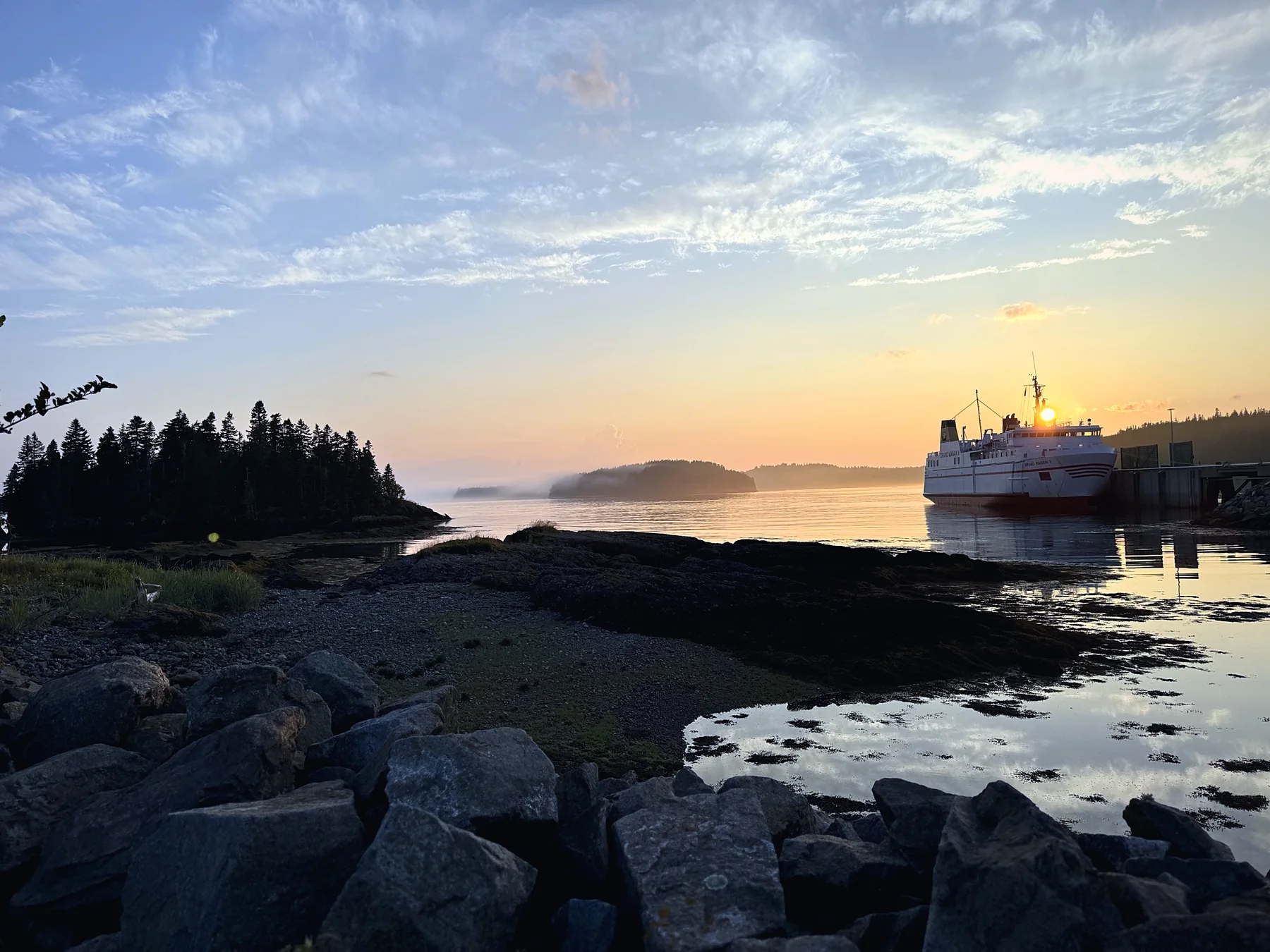 Sunset over rocky shoreline with a ferry in the harbour